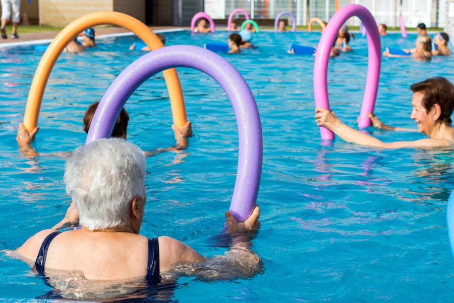 Senior women doing exercise with soft foam noodles in pool. Clube
